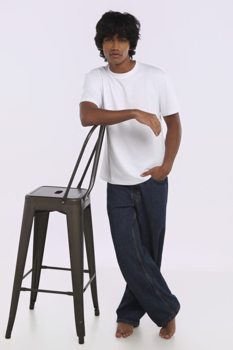 Shabs standing beside a stool in a white tee and denim